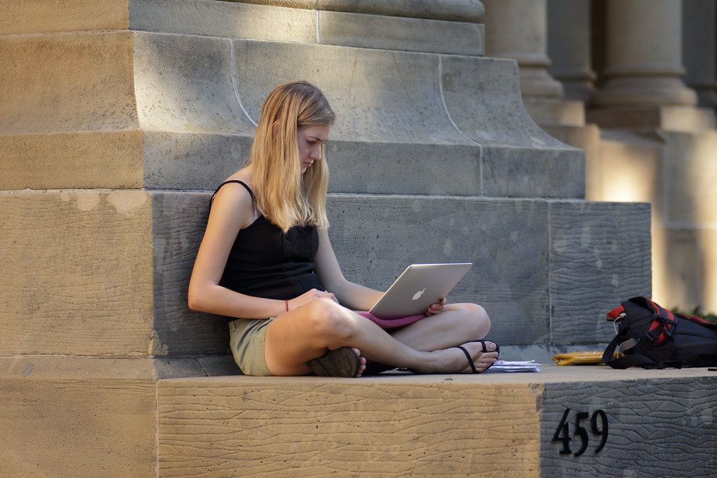 A university student working on a laptop on campus steps